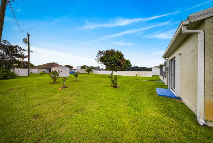 Expansive lawn space featuring established plantings, a privacy fence, and a neutral stucco exterior with white trim