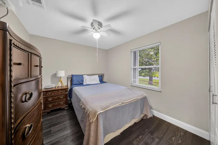 Interior room featuring dark wood-finish flooring, a ceiling fan with integrated lighting, a double-hung window, and a louvered closet door