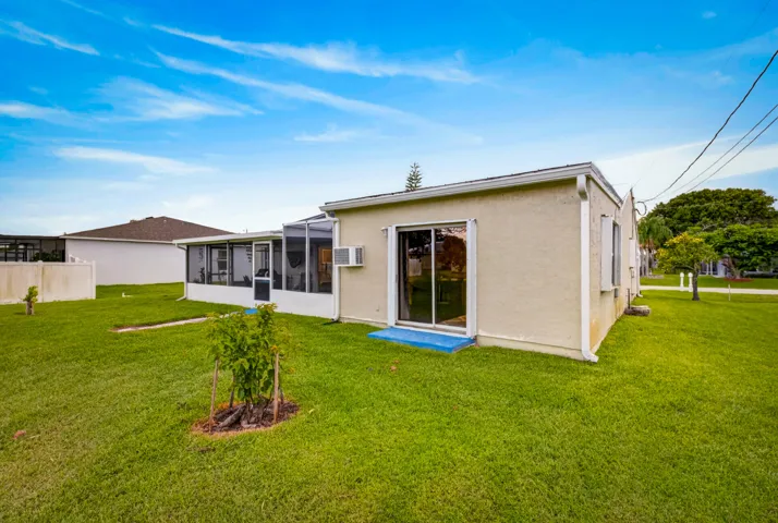 Expansive green lawn surrounds a stucco exterior property featuring a screened-in patio and sliding glass door entry