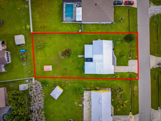 Property featuring a metal roof, expansive green lawn, mature trees, and a concrete driveway