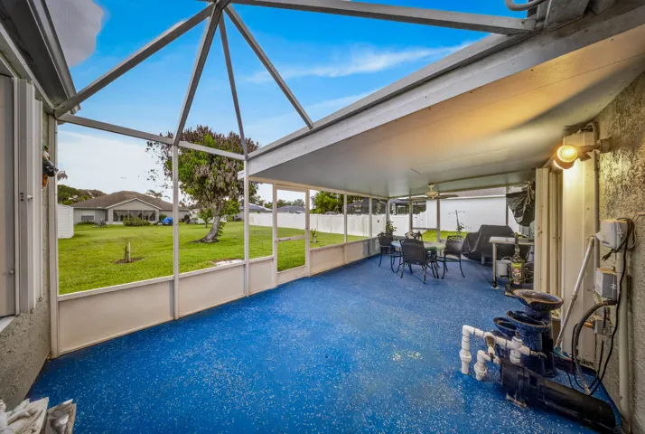 Screened patio with a textured blue floor, featuring an overhead fan, mounted exterior lighting, and a visible pool pump system