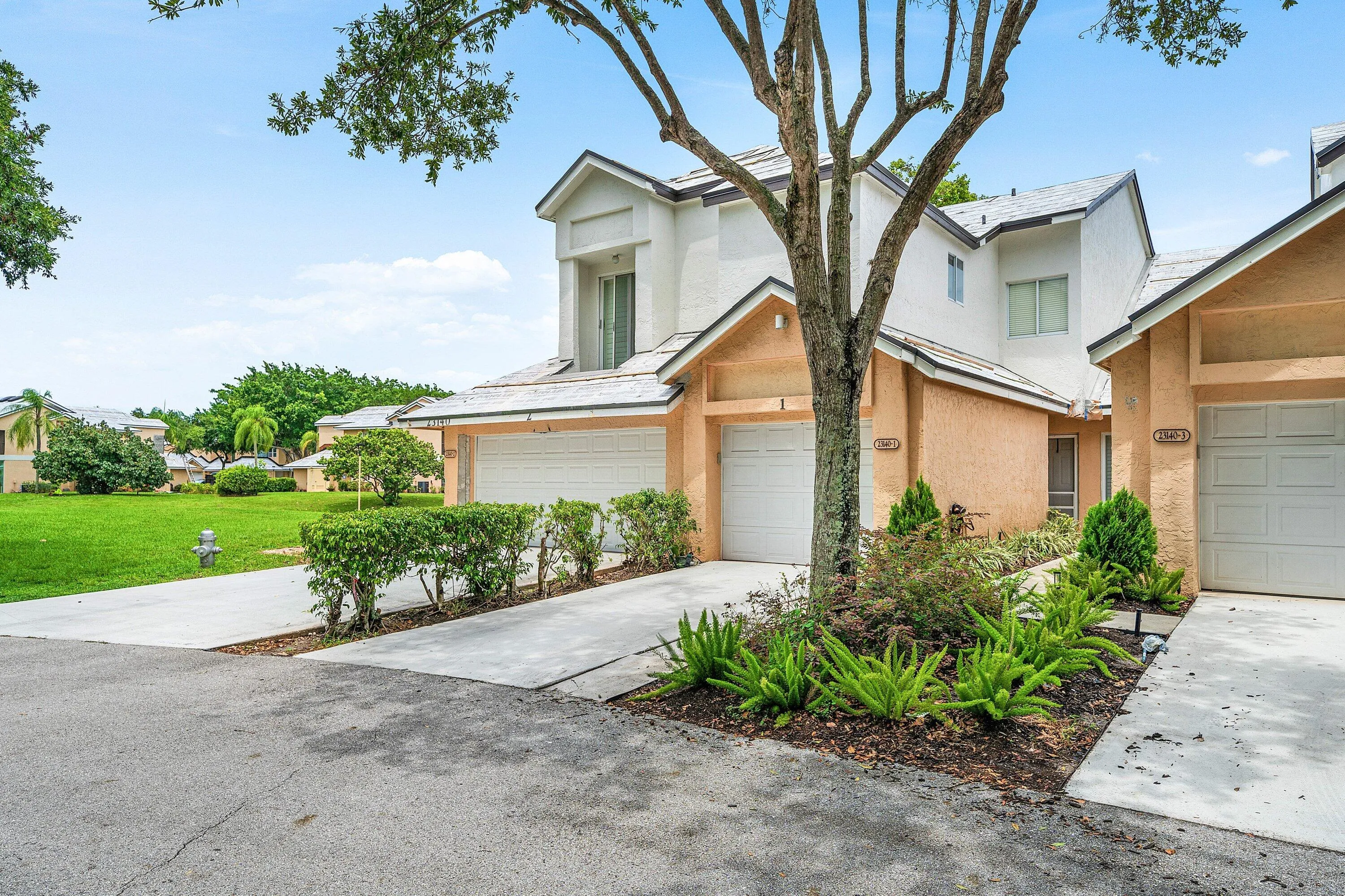 Exterior featuring a two-story stucco facade, gabled rooflines, an integrated single-car garage, mature tree, and landscaped planting beds
