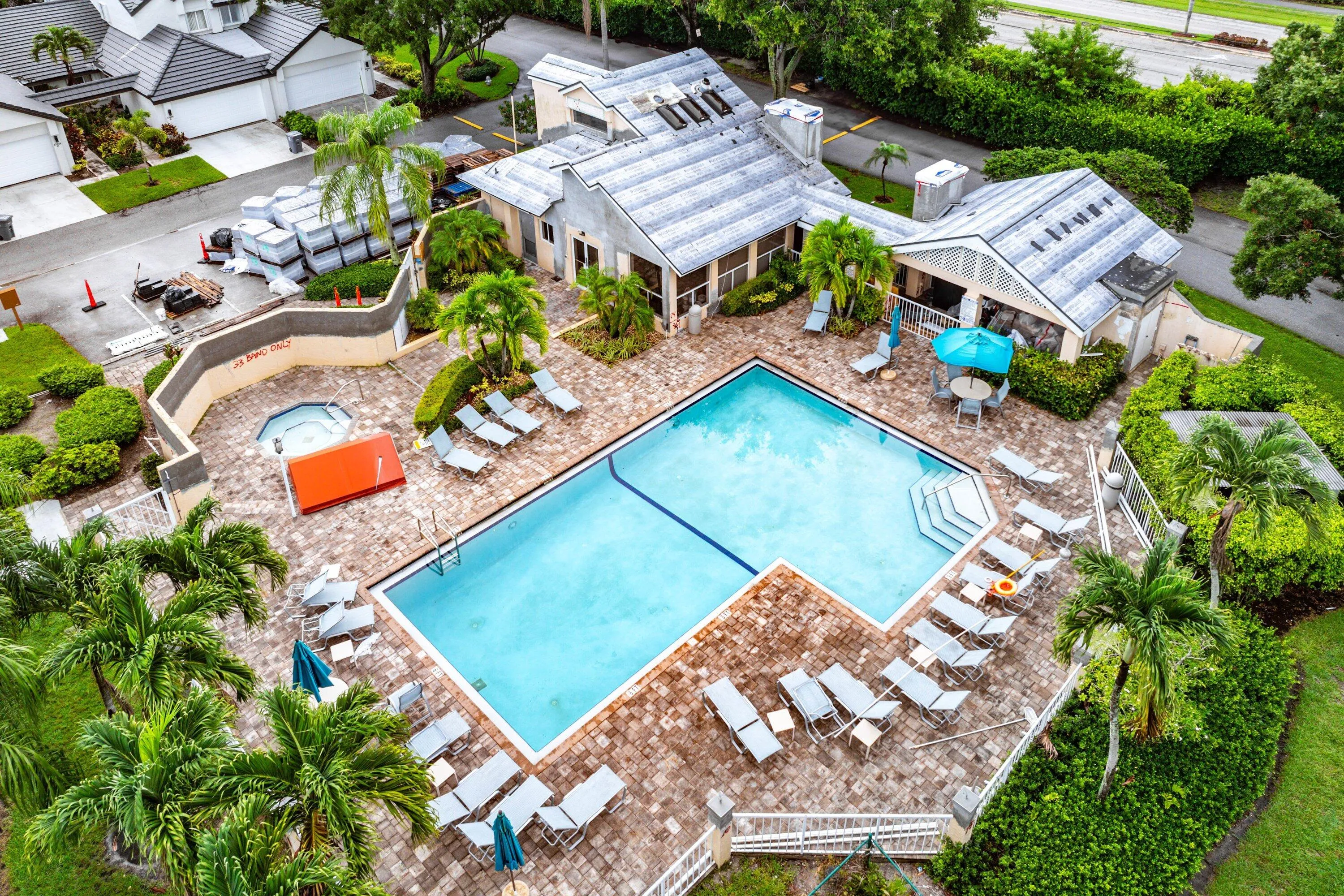 Community pool area featuring a rectangular swimming pool with integrated steps, surrounding paver patio, and mature palm trees