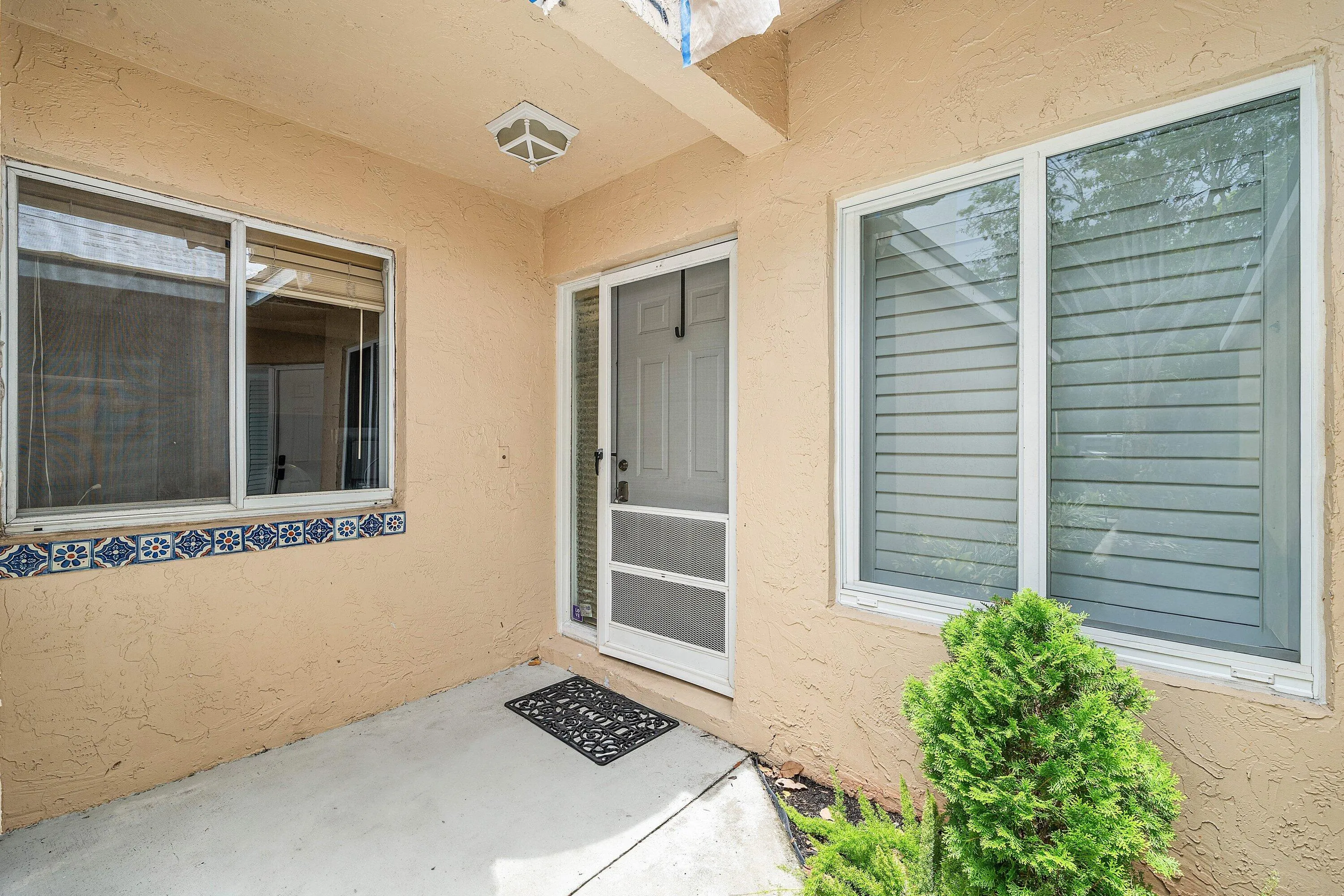 Covered entry featuring a textured stucco exterior, decorative tile accents, and a screen door