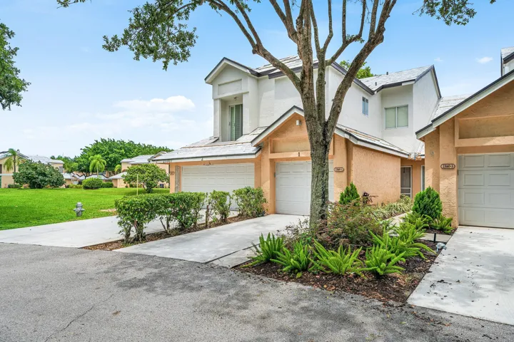 Exterior featuring a two-story stucco facade, gabled rooflines, an integrated single-car garage, mature tree, and landscaped planting beds