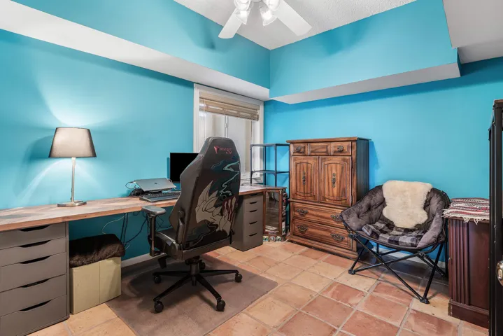 Room featuring vibrant blue walls, terracotta-style floor tiles, a window with blinds, and a ceiling fan