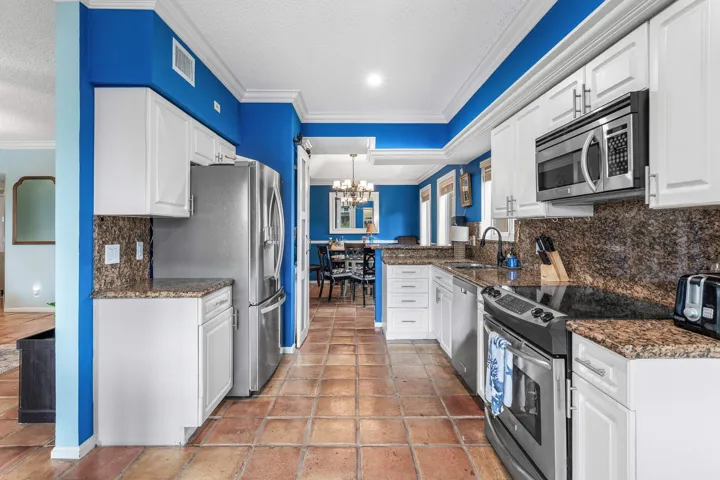 Galley kitchen featuring white cabinetry, stone countertops, stainless steel appliances, tile flooring, and crown molding