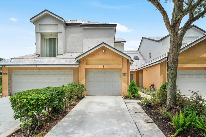 Stucco exterior with multiple white garage doors, a concrete driveway, and mature landscaping