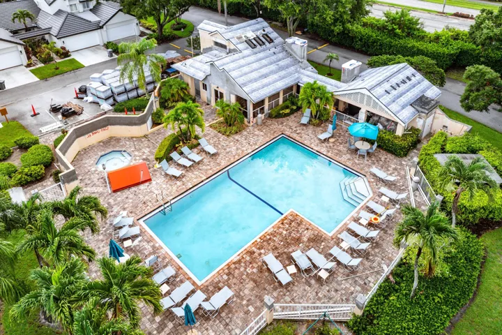 Community pool area featuring a rectangular swimming pool with integrated steps, surrounding paver patio, and mature palm trees