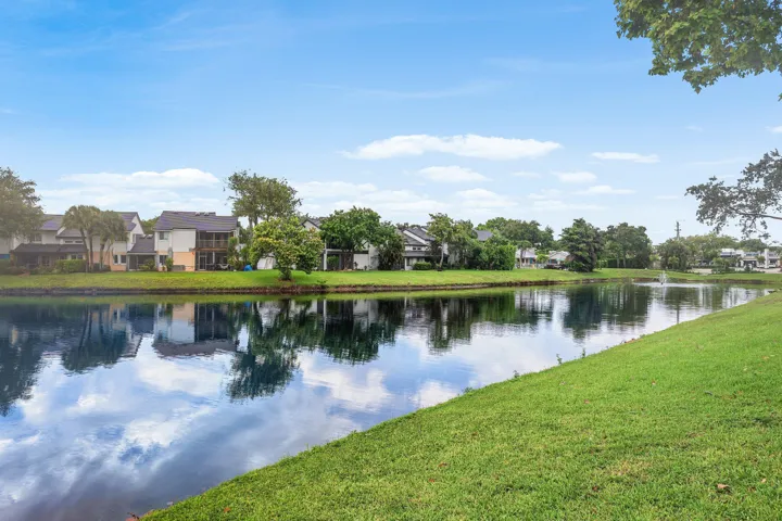 Waterfront property featuring a serene pond with a fountain, lush green grass, and mature trees