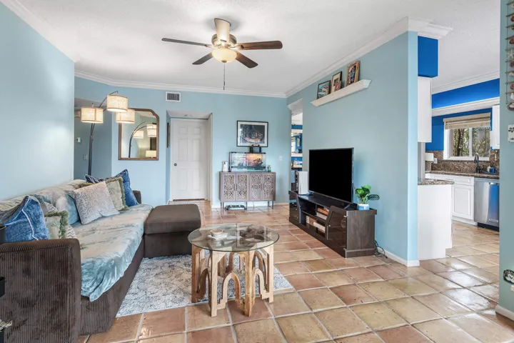 Spacious living area featuring terra cotta tile flooring, crown molding, and a ceiling fan