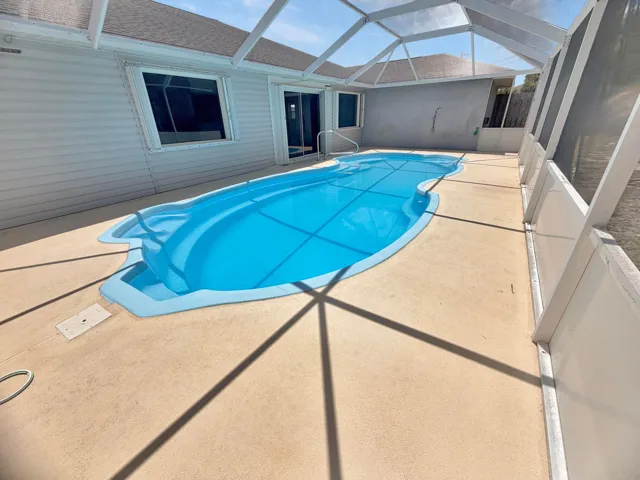 Screened enclosure featuring a freeform pool with integrated steps, a concrete pool deck, and a white vinyl-sided exterior