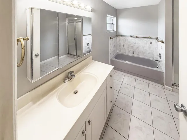 Bathroom featuring a single vanity with built-in sink, three-panel mirrored medicine cabinet with integrated lighting, a tub with tiled surround, and a separate shower enclosure