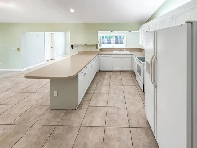 Kitchen featuring an extensive island with countertop seating, white cabinetry, light-toned tile flooring, and a window above the sink