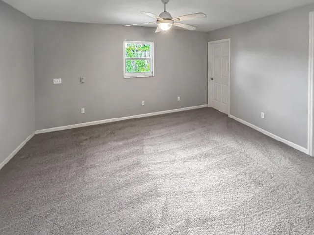 Carpeted room featuring a ceiling fan with integrated lighting, a double-hung window, and a paneled interior door