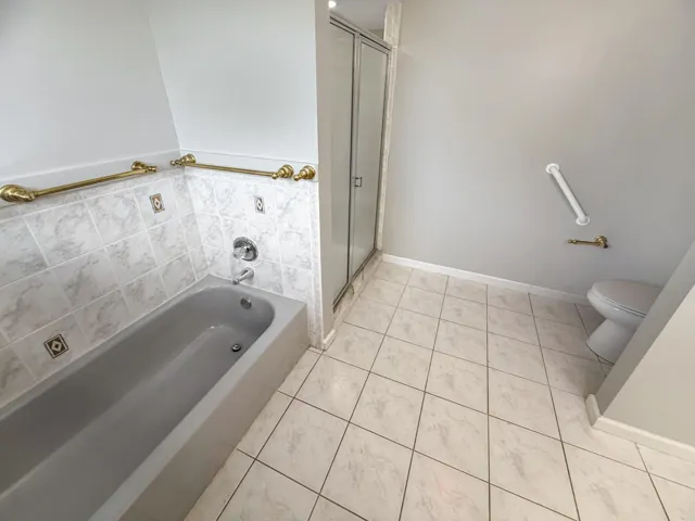 Full bathroom featuring a tub with surrounding wall tiling, a separate shower enclosure with a glass door, and square floor tiles