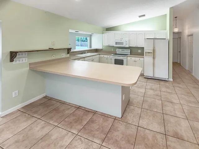 Kitchen featuring a peninsula counter with ample space, white cabinetry, and white appliances