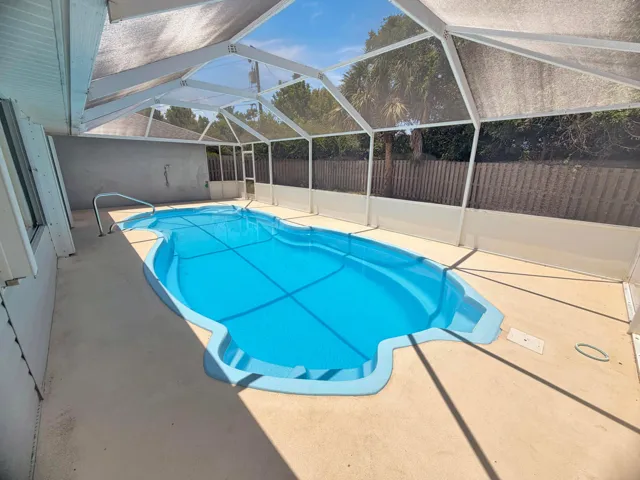 Screened outdoor pool area featuring a freeform pool with integrated steps, a concrete patio surround, and a white screen enclosure with a pitched roof