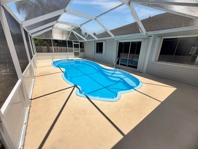 Screen-enclosed pool area with a freeform swimming pool featuring integrated steps and a handrail
