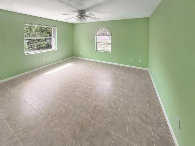 Spacious room featuring neutral tile flooring, two windows providing natural illumination, and a ceiling fan fixture