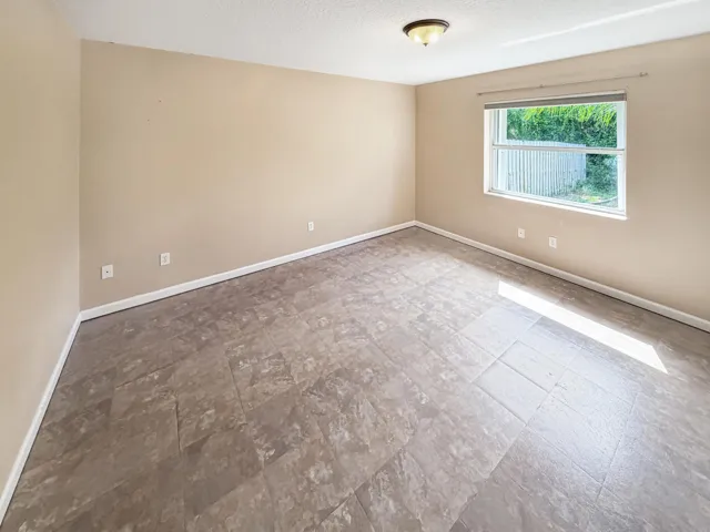 Spacious room featuring textured flooring, neutral wall tones, a large window, white baseboards, and a ceiling-mounted light fixture