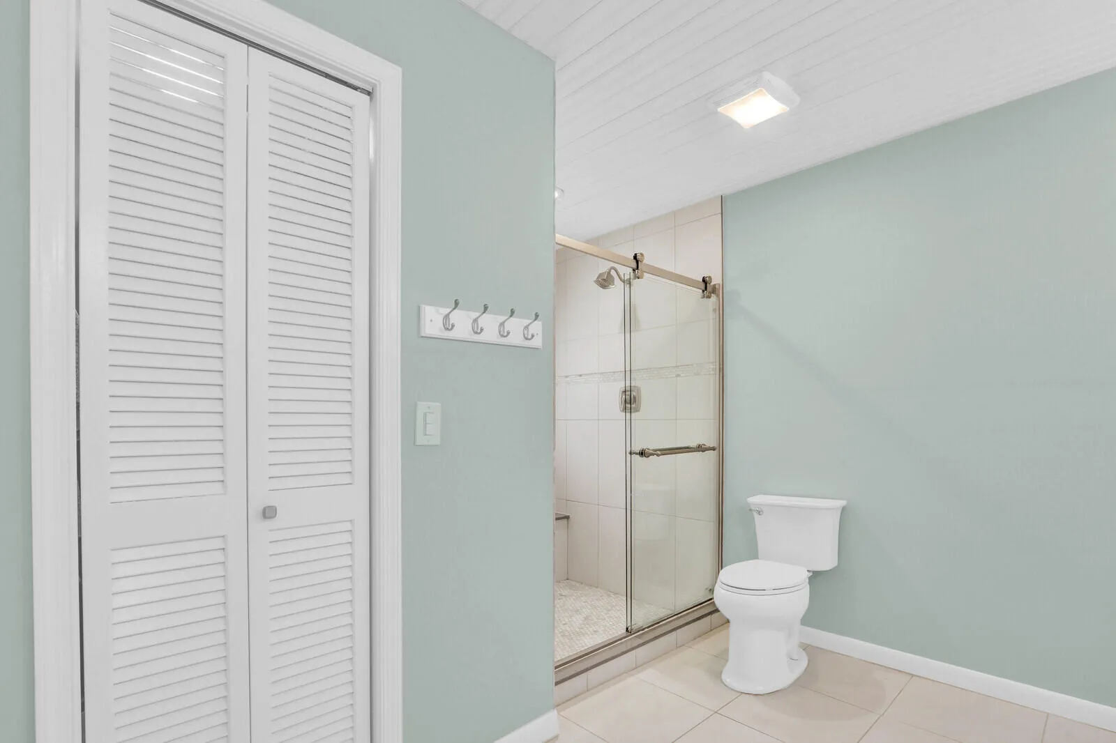 Bathroom featuring a glass-enclosed shower with tile surround, a white toilet, and light-toned floor tiling