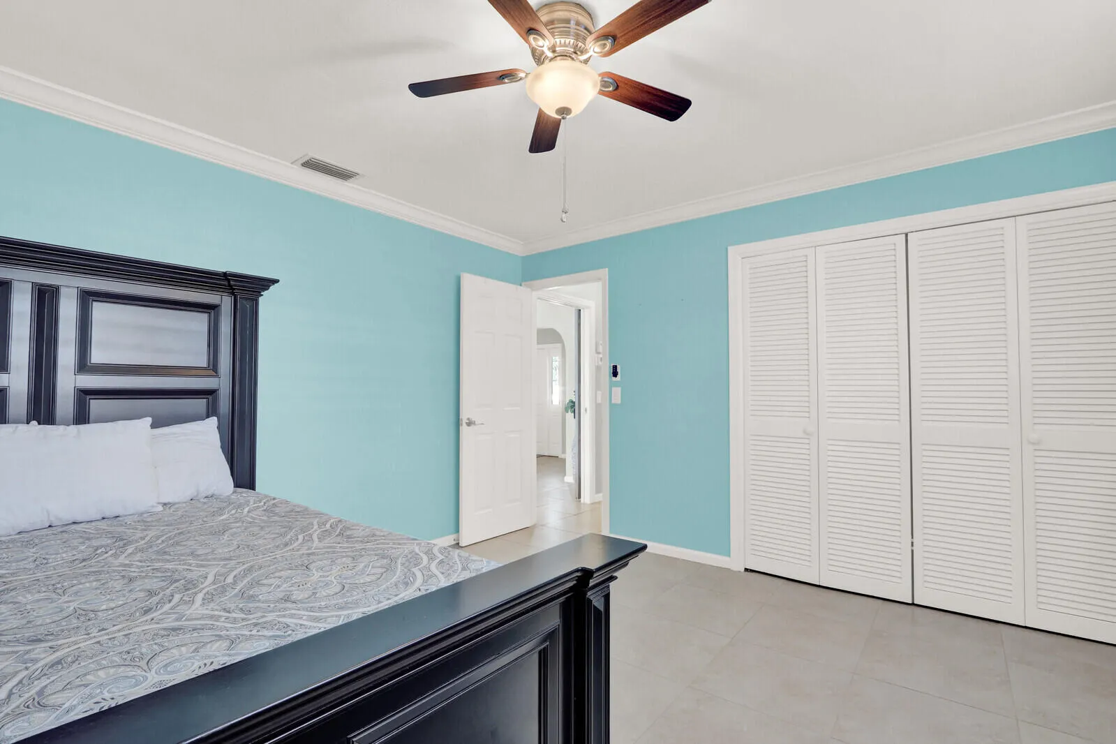 Light blue walls with white crown molding, a ceiling fan with light fixture, and white louvered closet doors