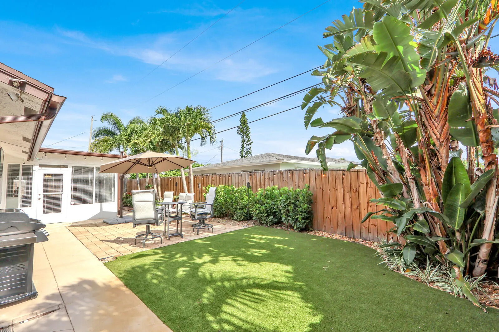 Private backyard with artificial turf, a paved patio area, and mature tropical landscaping