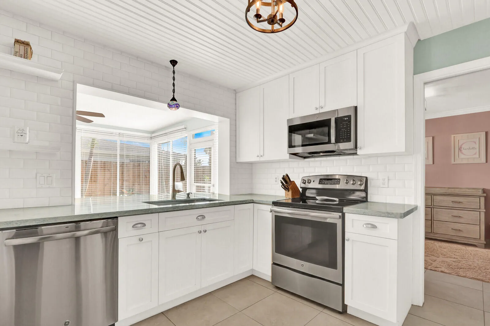 Modern kitchen featuring white shaker cabinetry, stainless steel appliances, a subway tile backsplash, and a pass-through window
