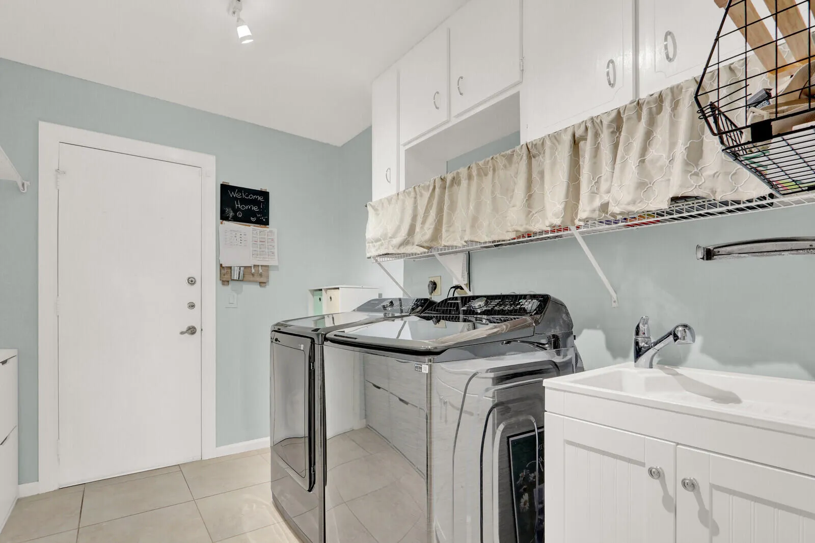Dedicated laundry area featuring white upper cabinetry, a utility sink with a white vanity, and light-toned tile flooring