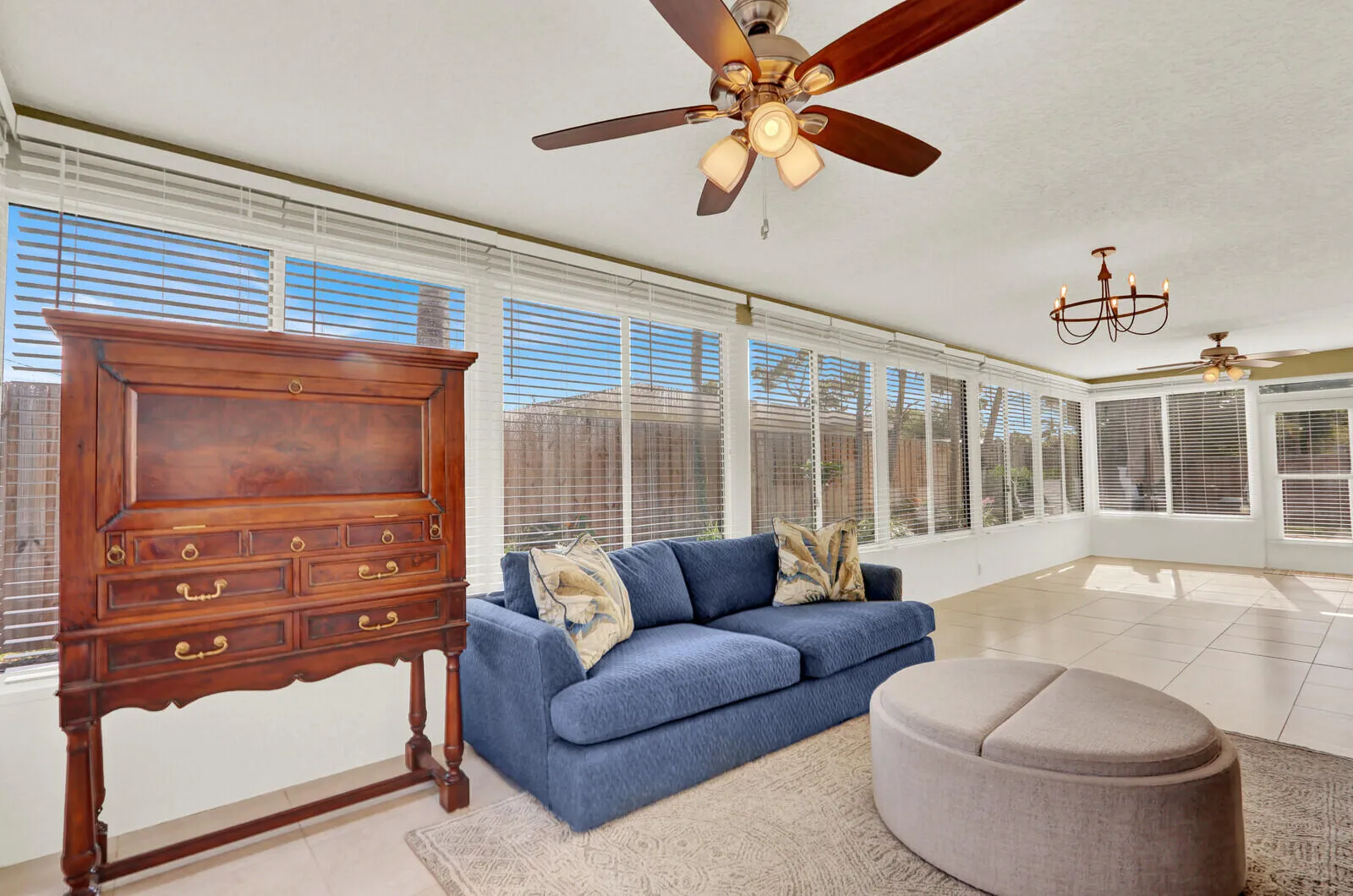 Sunroom featuring expansive window walls with horizontal blinds, neutral tile flooring, and multiple ceiling fans