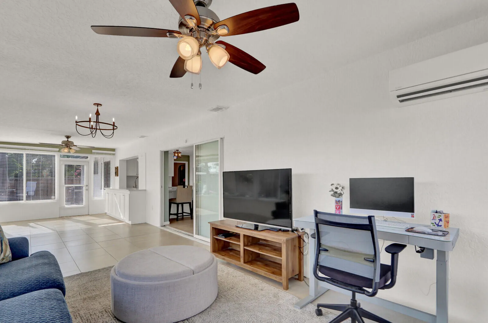 Living area with tile flooring, a ceiling fan with integrated lighting, and a wall-mounted mini-split unit