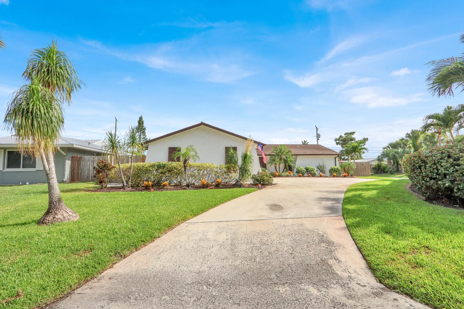 Front exterior featuring a concrete driveway, manicured lawn, and mature tropical landscaping