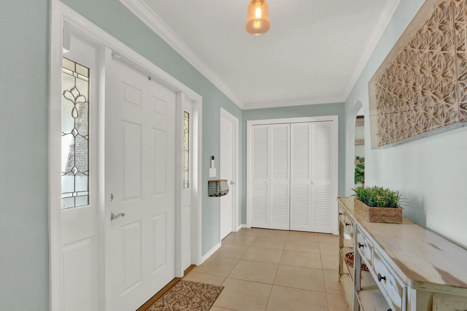 Entryway featuring a paneled door with decorative sidelight windows, light-toned tile flooring, louvered bi-fold closet doors, and crown molding