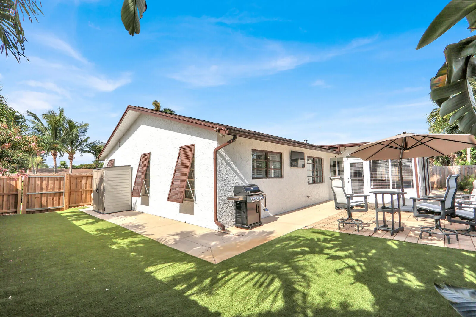 Expansive outdoor area featuring a combination of artificial turf and concrete patio, a privacy fence, and mature palm trees