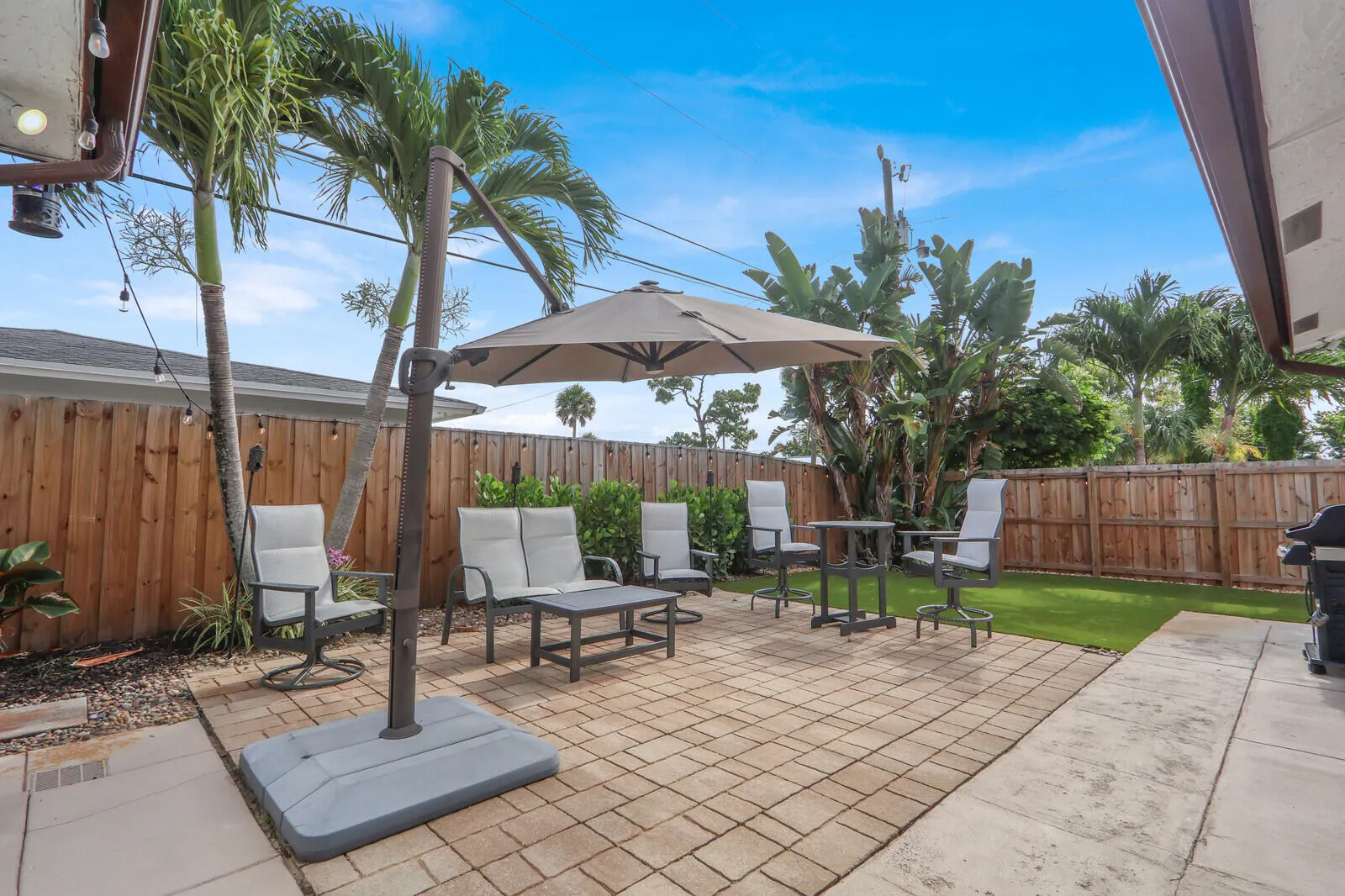Paver patio with a large offset patio umbrella, privacy fencing, and tropical landscaping