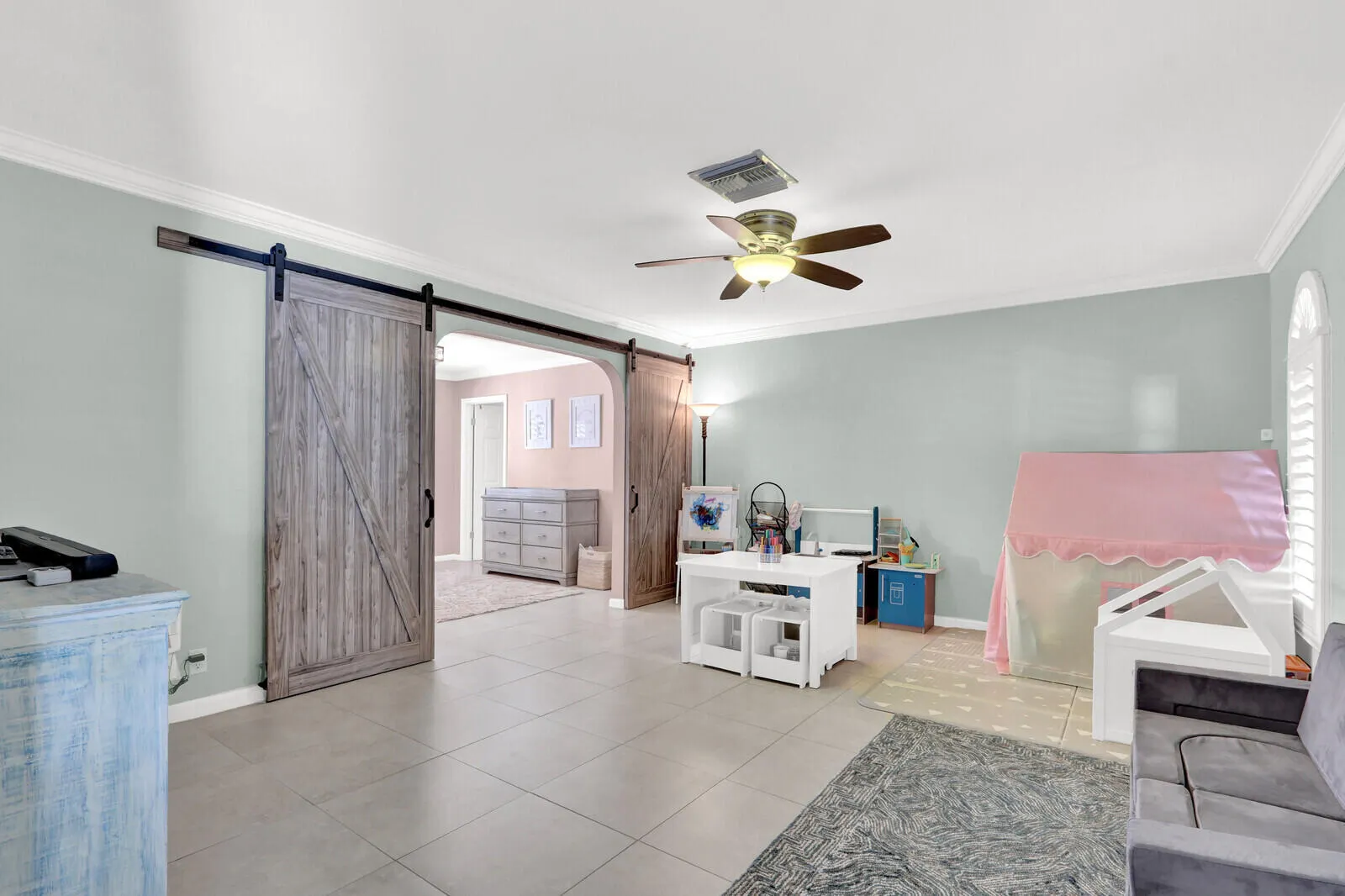 Interior space featuring wood-finish barn doors, a ceiling fan with integrated lighting, crown molding, and neutral tile flooring