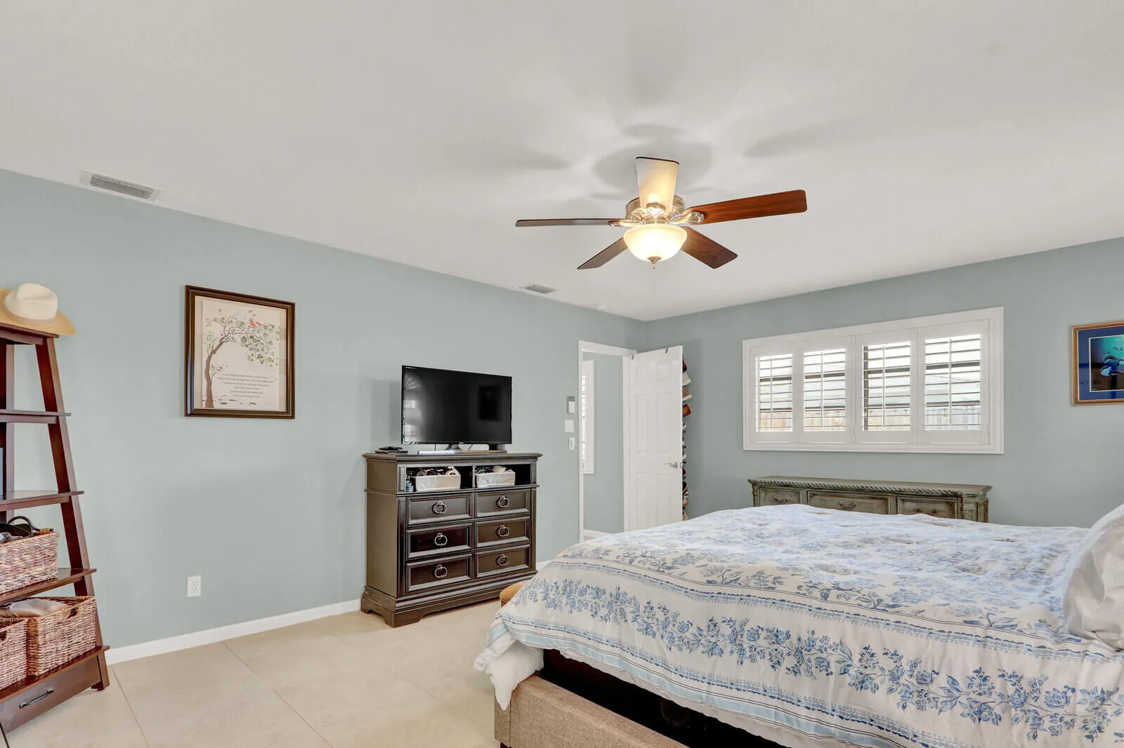 Room featuring tile flooring, ceiling fan with light fixture, window with plantation shutters, and a white paneled door