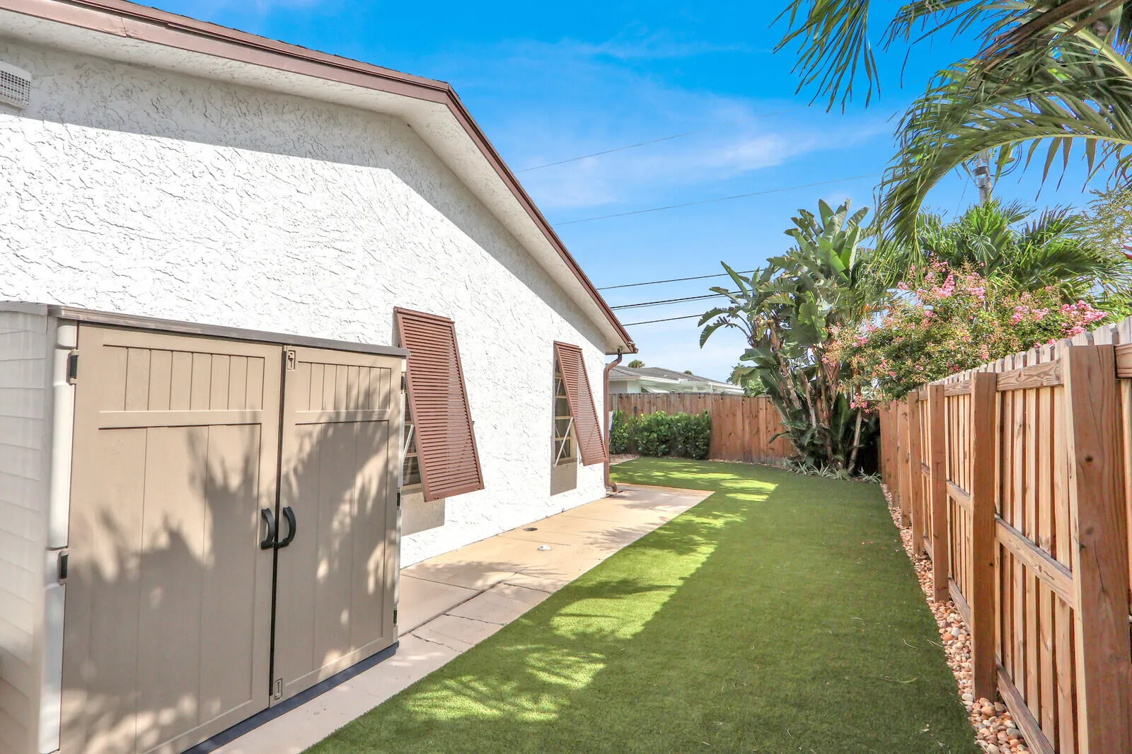 Exterior side yard featuring a durable privacy fence, artificial turf, and a concrete pathway