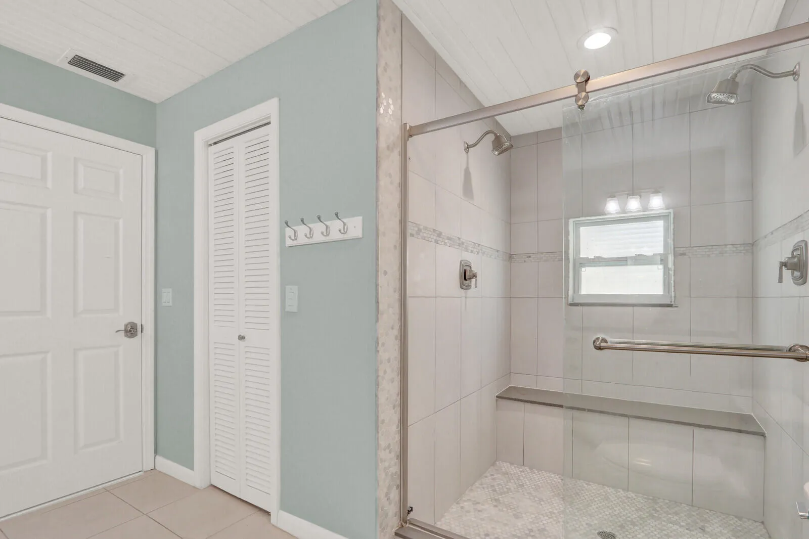 Glass-enclosed shower featuring dual showerheads and a built-in bench