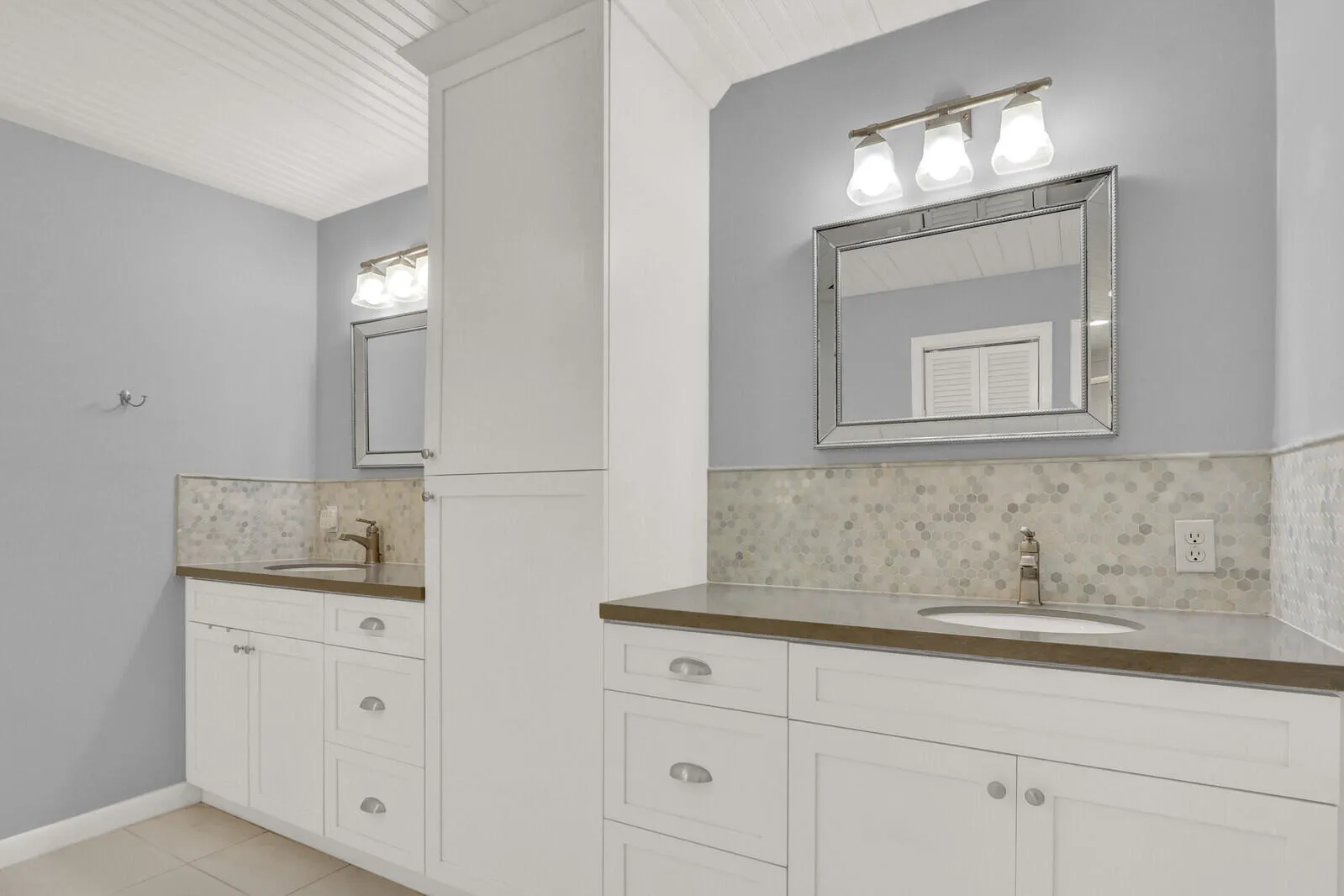 Dual vanity bathroom featuring white cabinetry, integrated sinks, solid surface countertops, and mosaic tile backsplash