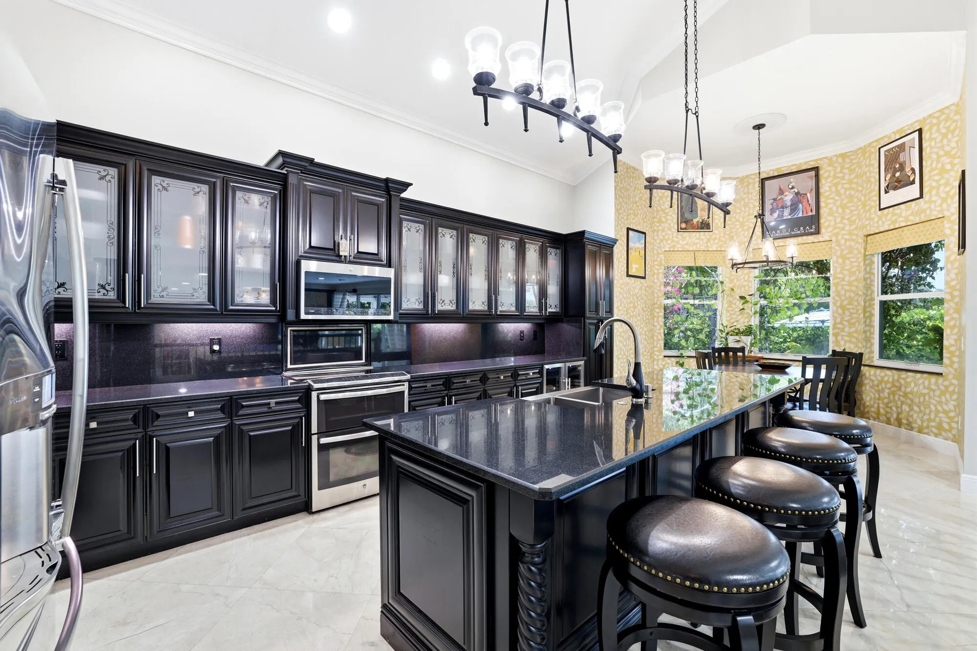 Gourmet kitchen featuring dark cabinetry with glass-front uppers, stainless steel appliances, dark stone countertops, and a central island with integrated sink