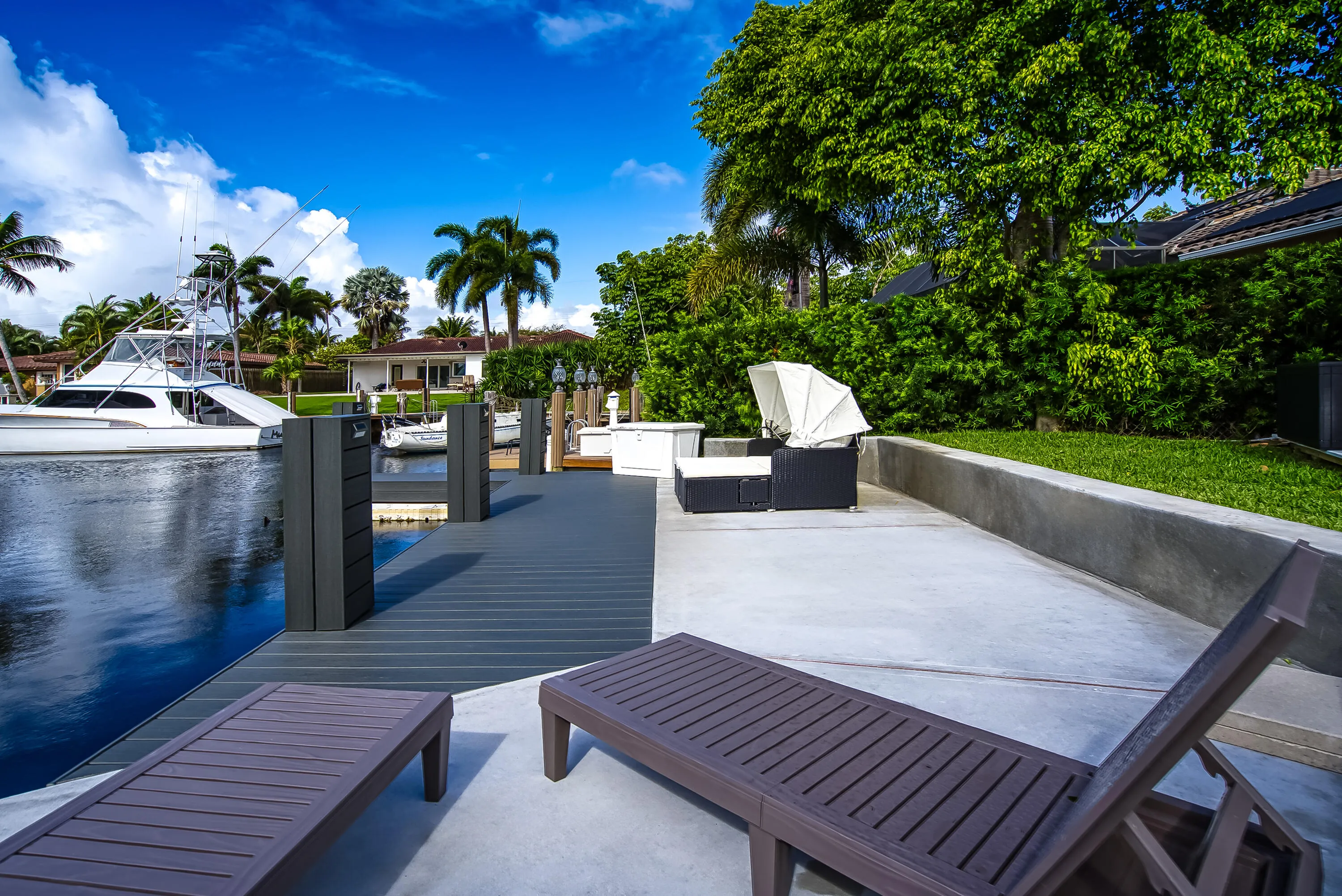 Waterfront property featuring a private boat dock, concrete patio, and lush green landscaping