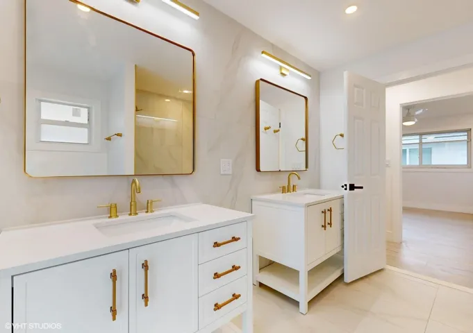 Two separate vanities with mirrors provide individualized storage spaces and places for toiletries for its bathroom users