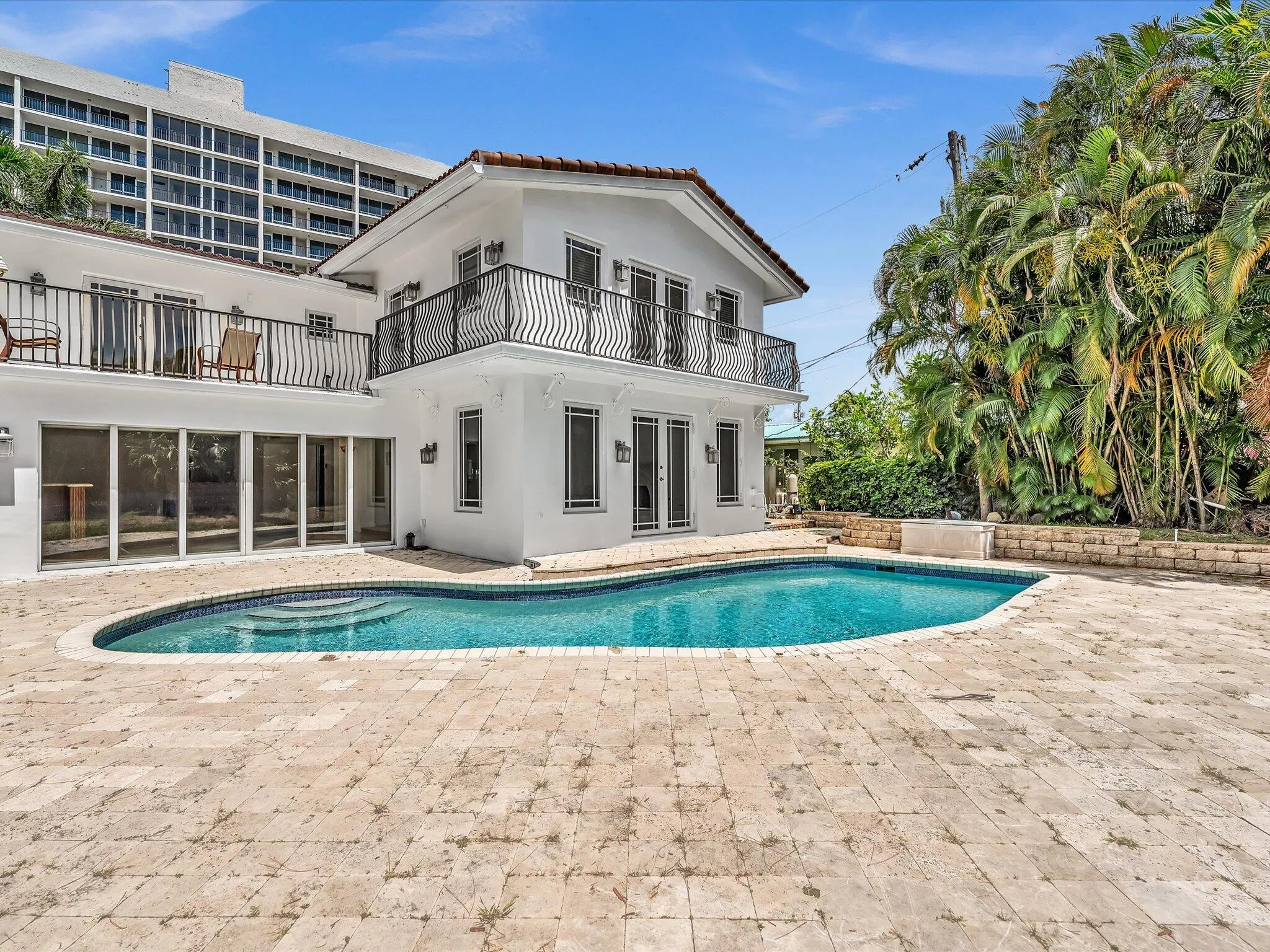 Rear exterior featuring a freeform pool with integrated steps, surrounded by a large paver patio