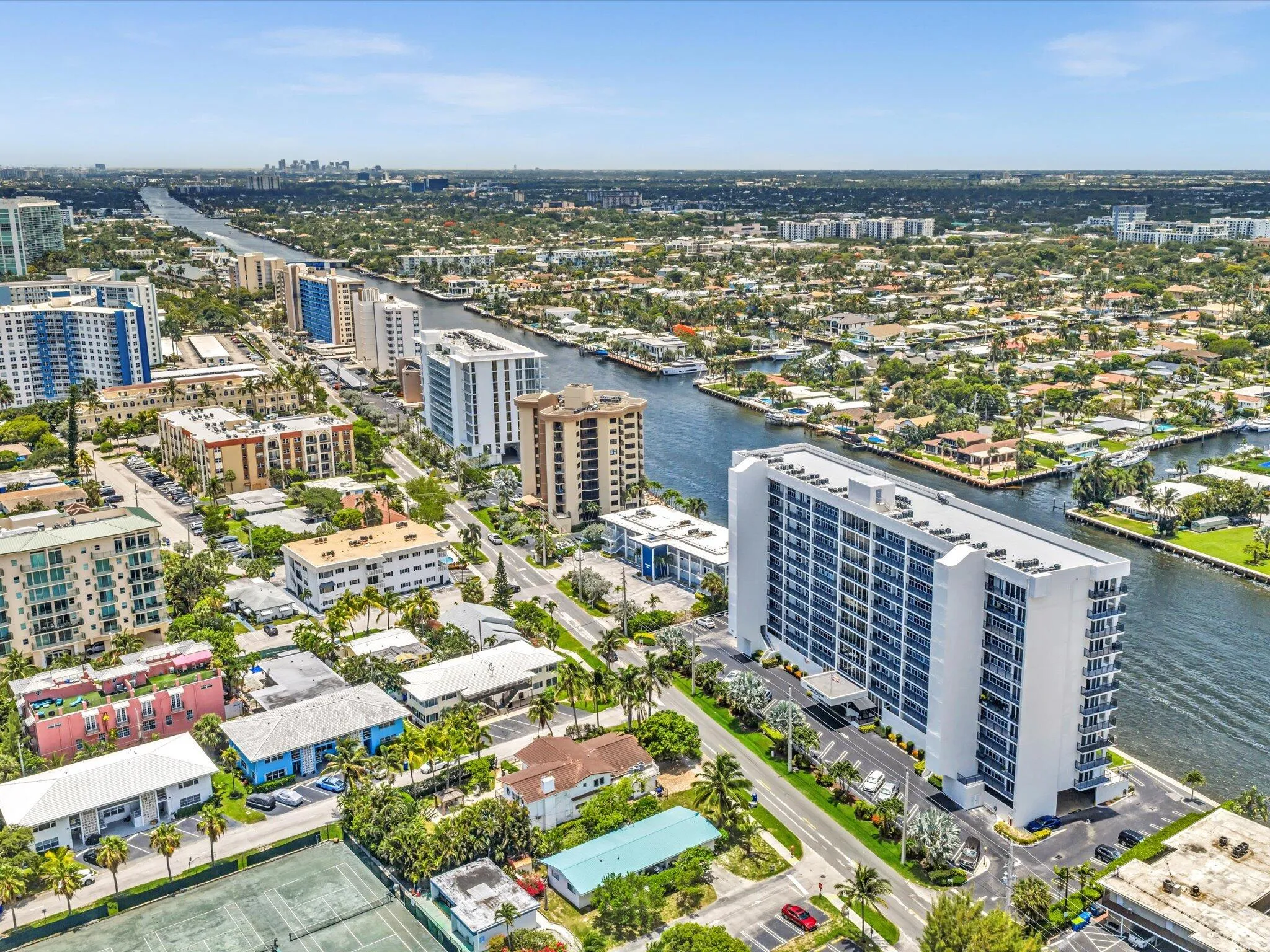 High-rise residential building featuring multiple balconies, a surrounding paved parking area, and manicured landscaping