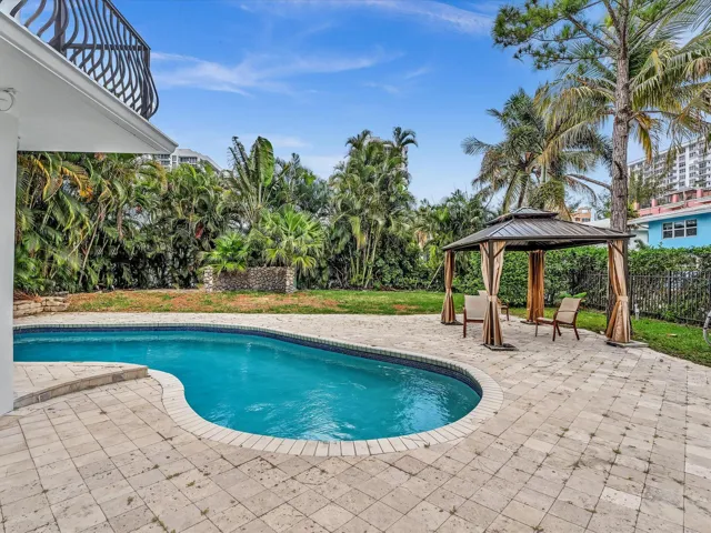 Outdoor oasis featuring a free-form swimming pool with a paved patio surround, a shaded gazebo, and mature tropical landscaping