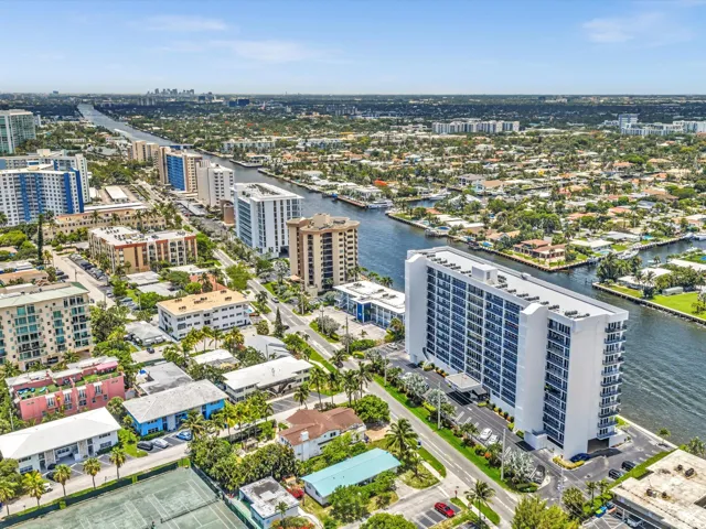 High-rise residential building featuring multiple balconies, a surrounding paved parking area, and manicured landscaping