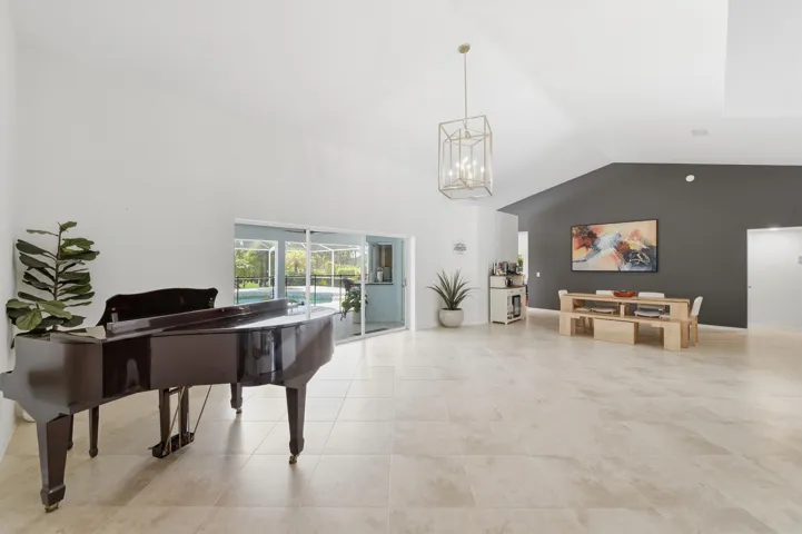 Spacious interior featuring vaulted ceilings, light-toned tile flooring, a modern geometric chandelier, and sliding glass doors opening to a screened outdoor pool area