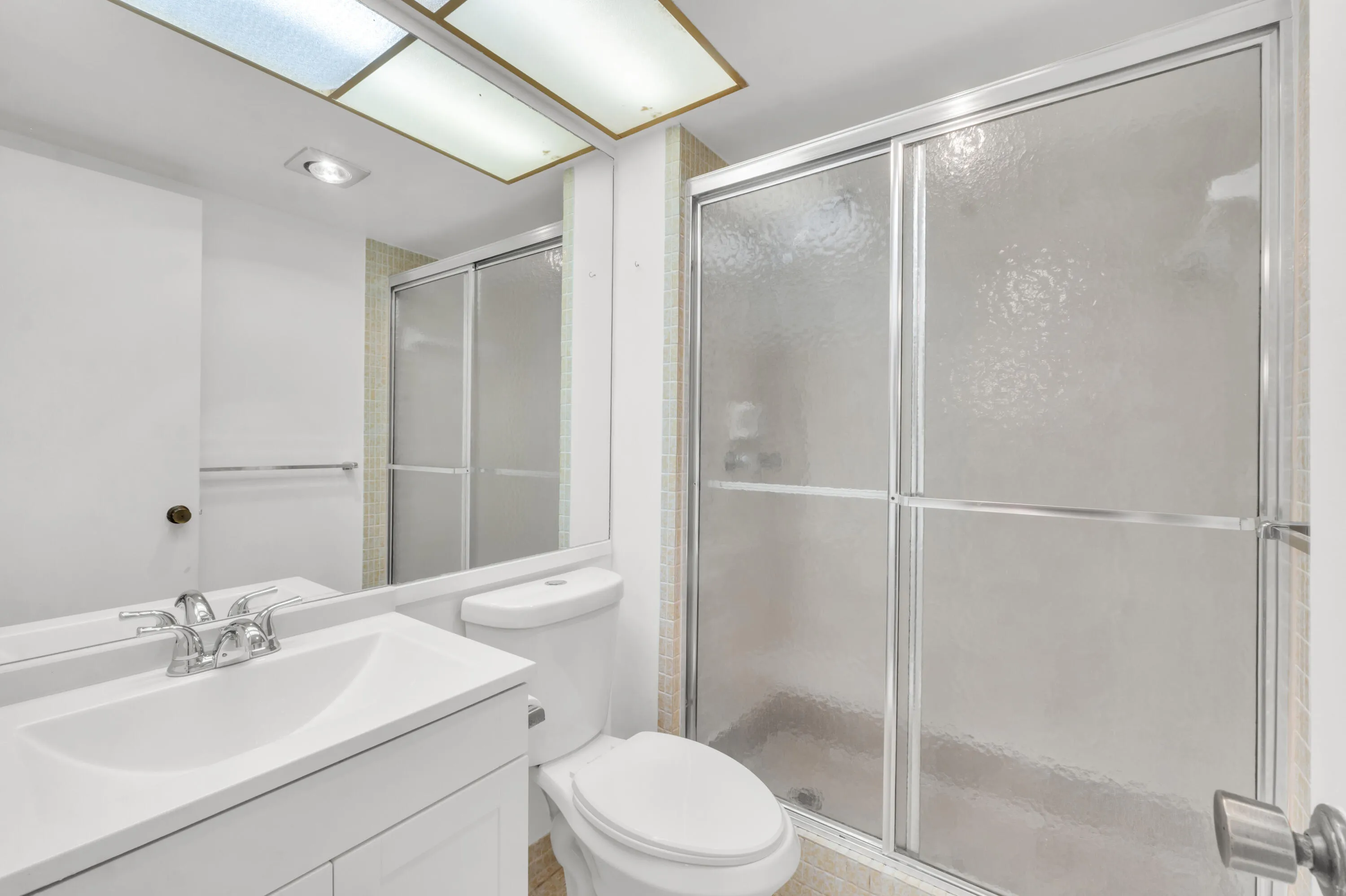 Guest bathroom featuring a newer white vanity with integrated sink, chrome faucet, mirrored wall, and a shower enclosure with frosted glass sliding doors